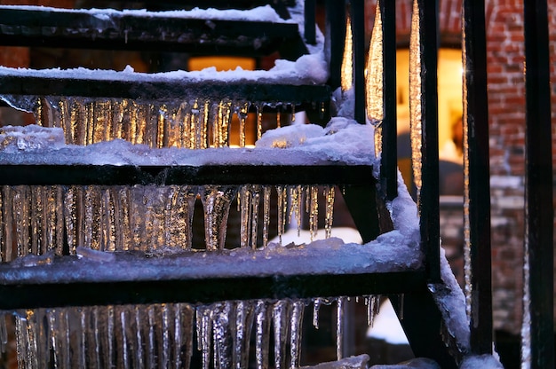 outdoor staircase at evening twilight covered with ice and icicles lit by a window behind it