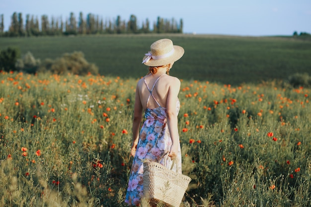 Outdoor summer portrait of teen girl with basket strawberries, straw hat. A girl on country road, back view. Nature background, rural landscape, green meadow, country style