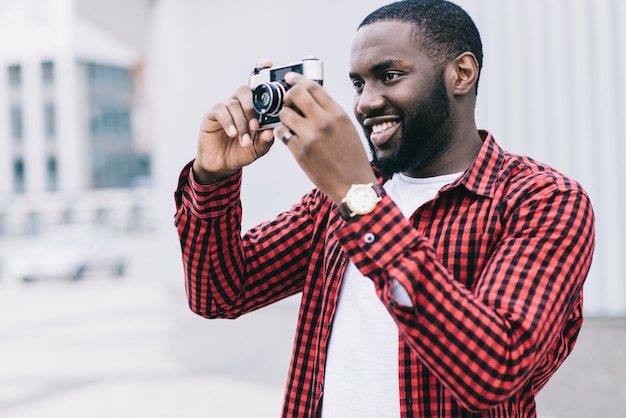 屋外の夏の笑顔のライフスタイル肖像画ハンサムで幸せアフロアメリカの観光客がカメラでヨーロッパの街で楽しむ旅行写真のヒップスタースタイルで写真を撮る