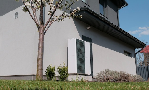 Outdoor unit of a heat pump against the wall of a modern cottage