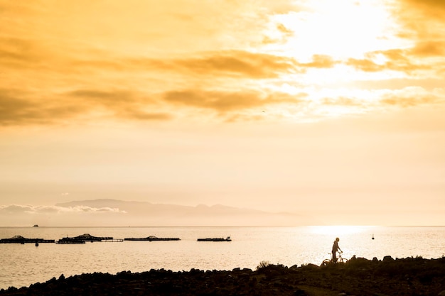 Outdoor vrijetijdsbesteding met man en mountainbike in silhouet met gouden en gekleurde zonsondergang in achtergrond oceaan en kust wolken en sport concept vakantie zomer stijl