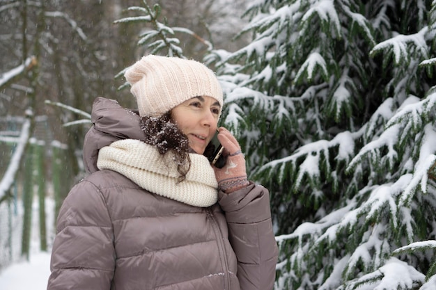 屋外の冬の肖像画。雪に覆われた冬の公園で携帯電話で話している45歳の美しい女性。