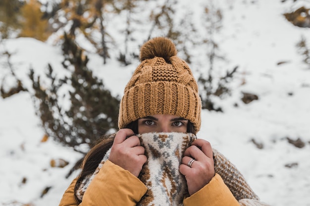 outdoor winter portrait of young woman wearing winter clothes holding scarf over her mouth and nose