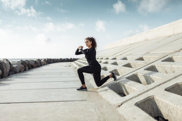 Outdoor workout concept Fit slanke vrouw met krullend haar strekt zich uit of warmt op op een stedelijke dijk met betonnen platen