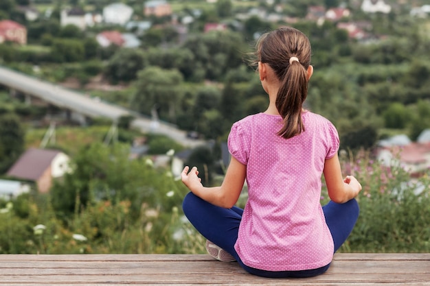 Allenamento all'aperto ragazza yoga bambino seduto posizione del loto sullo sfondo della natura