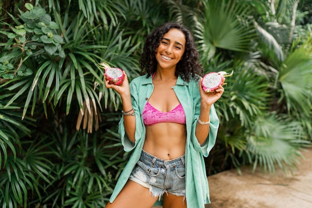 Outdoor zomer foto van lachende mooie brunette vrouw met golvende haren met tropisch fruit