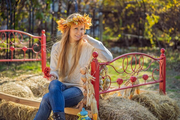 アウトドア ライフ スタイルは、秋の葉の花輪を身に着けている魅力的な金髪の若い女性の肖像画を間近しますスタイリッシュなニット プルオーバーを着てカエデの葉の花輪