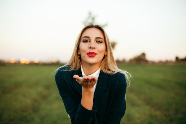 Outdoors lifestyle fashion portrait of happy stunning blonde girl smiling and kissing to cameta