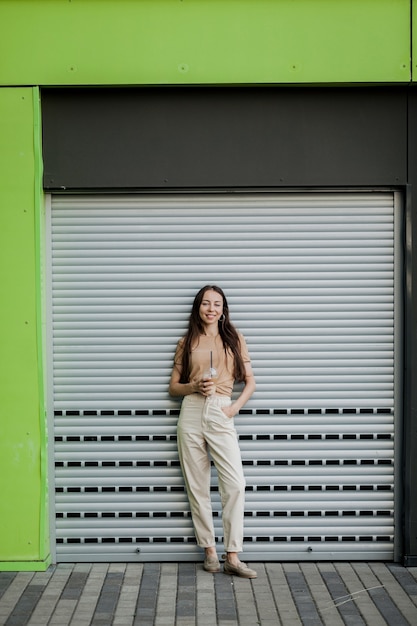 Outdoors lifestyle fashion portrait of stunning girl. Smiling, drinking coffee and walking on the city street.