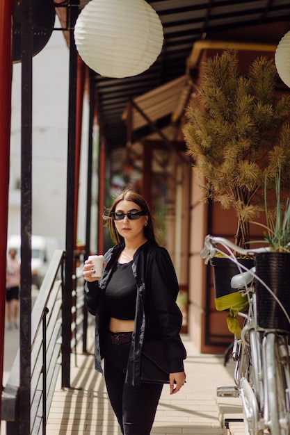 Outdoors lifestyle portrait of stunning brunette girl. Drinking coffee and walking on the city street.