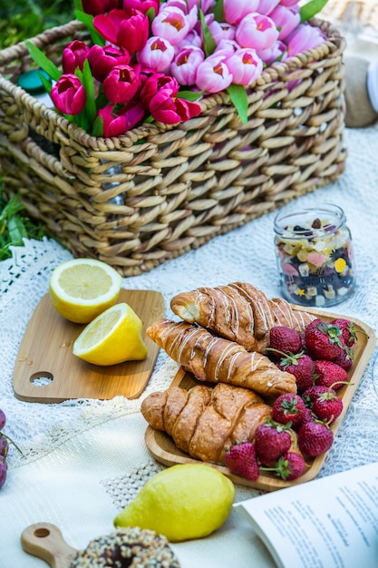 Пикник на свежем воздухе в пышном зеленом парке с вкусными круассанами, пончиками, фруктами и вином на траве