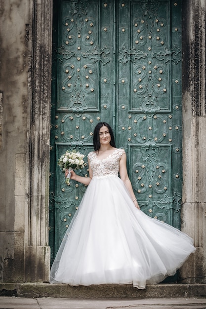 Outdoors portrait of beautiful young bride in luxurious white dress over old door