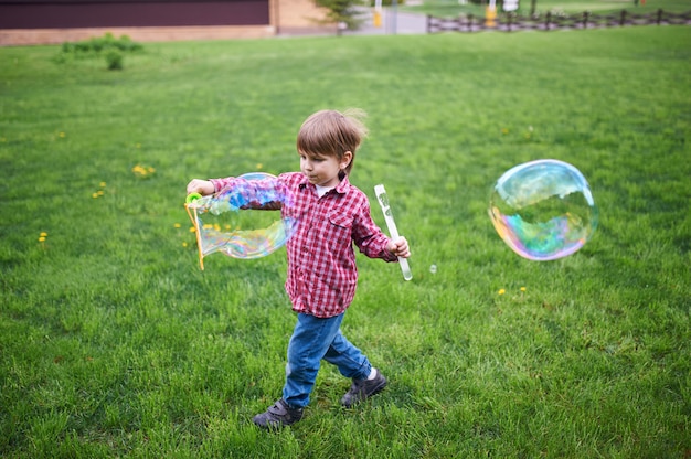 Outdoors portrait of cute preschool boy blowing soap bubbles on a green lawn