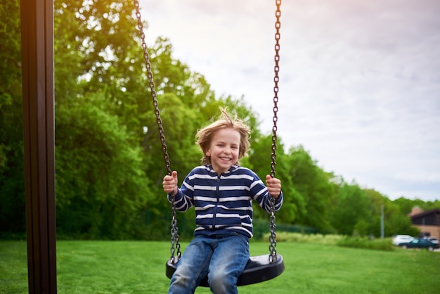 Outdoors portrait of cute preschool laughing boy swinging on a swing at the playground