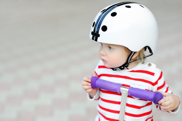 Photo outdoors portrait of cute toddler boy in safety helmet with scooter