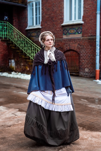 Фото На открытом воздухе портрет молодой викторианской женщины, идущей по старому городу