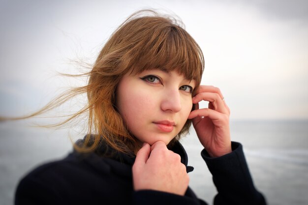 Outdoors portrait of young beautiful girl with red cheeks in winter near the frozen lake