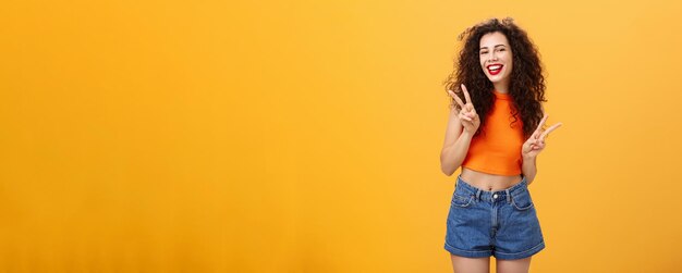 Outgoing friendlylooking attractive young female with curly haircut in cropped top and shorts showin