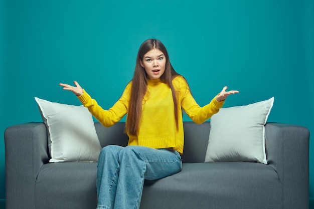 Outraged shocked girl asking what spreading hands in astonishment feeling discontent sitting on sofa