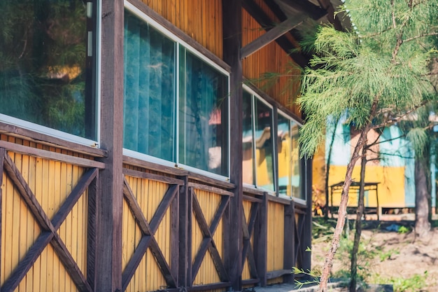 Outside view facade wooden yellow brown boards material country\
house panoramic window glass nature reflect curtains inside summer\
day warm light mood cozy home interiors leisure eco building