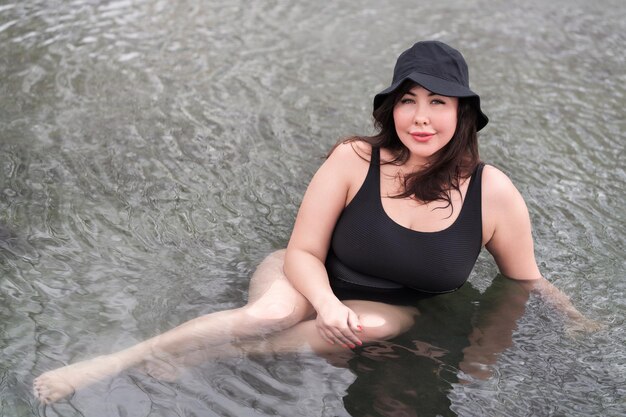 Outsize model in black swimsuit and panama lying relaxation in outdoors pool at spa resort