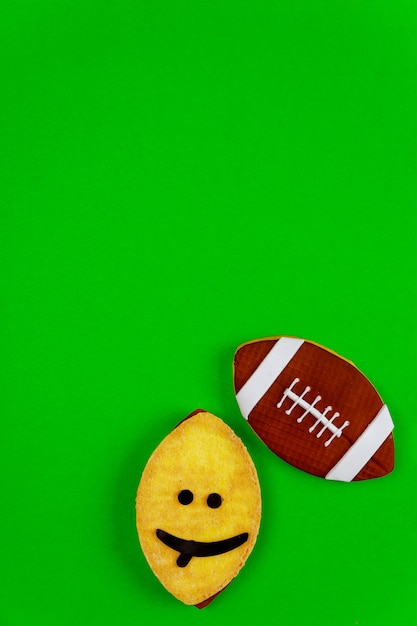 Oval funny face cookie as an american football ball isolated on\
green background. top view.