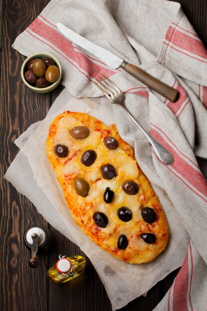 Oval pizza Greek with olives and with tomato on dark wooden rustic.   