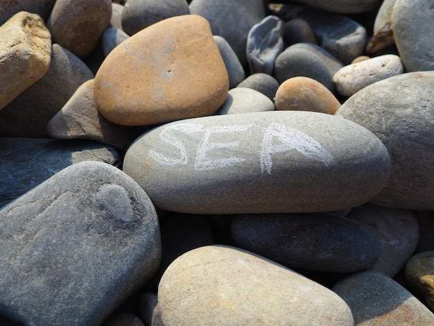 Oval stones large smooth sea pebbles illuminated by the summer sun The word sea is written on the stone Summer vacation in the resort wellness sea adventures and pleasure Stone gray background