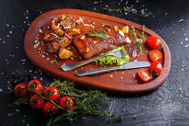 Oval wooden tray, kitchen cutting board, meat steak with vegetables, fried potatoes, spices