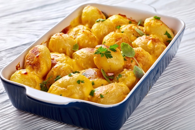 Oven baked cheesy new potatoes with cheddar cheese butter sauce in a baking dish on a white wooden table