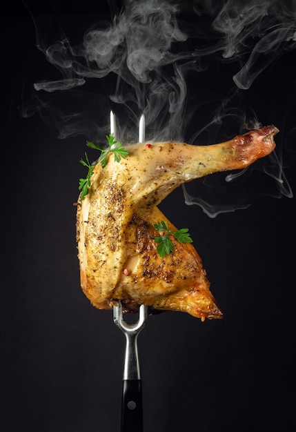 Oven baked chicken thigh with parsley on a fork Menu or recipe concept for restaurant or hotel on black background