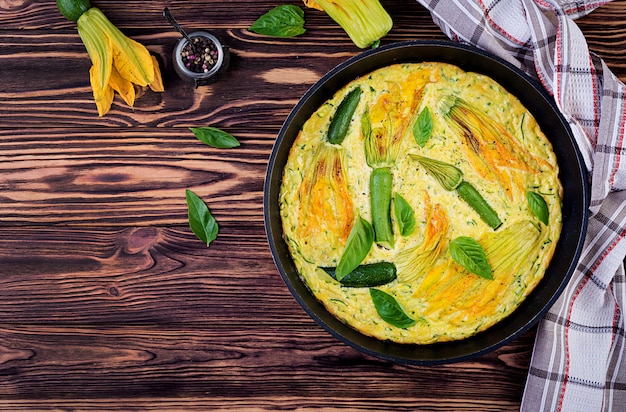Oven baked omelette with flowers zucchini in pan on wooden background