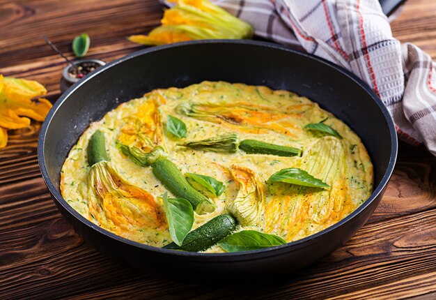 Oven baked omelette with flowers zucchini in pan on wooden background.