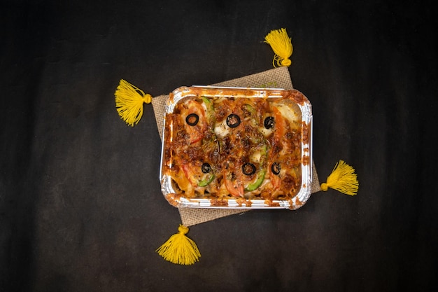 Oven Baked Pasta topping with olive tomato capsicum and cheese served in dish isolated on napkin dark background top view of indian fastfood