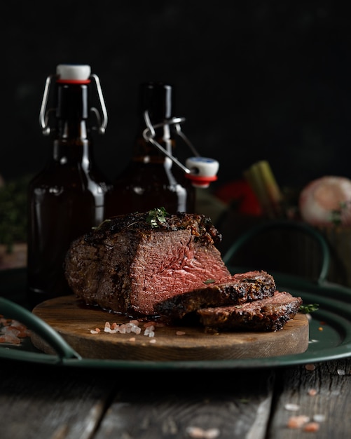 an oven-baked piece of roast beef and two bottles of dark beer on a green country-style iron tray