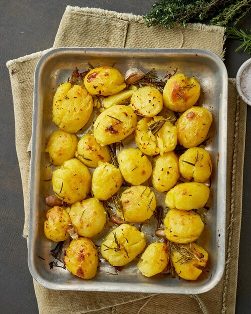 Foto patate al forno intere schiacciate e croccanti con condimenti ed erbe in vassoio metallico