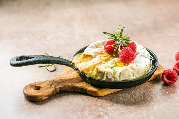 Ovengebakken camembertkaas met rozemarijnblaadjes en framboos Zelfgemaakte gegrilde brie op rustieke tafel