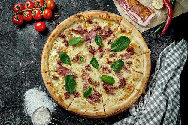 Ovengebakken Italiaanse pizza met saus, kaas, ham en zongedroogde tomaten in een compositie met ingrediënten op een donkere tafel. Uitzicht van boven