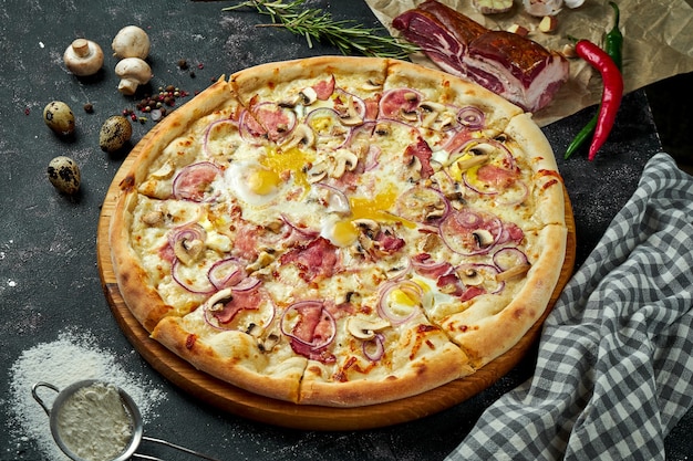 Ovengebakken Italiaanse pizza met witte saus, kaas, ham, champignons en rauwe dooiers in een compositie met ingrediënten op een donkere tafel. Uitzicht van boven. Pizza carbonara