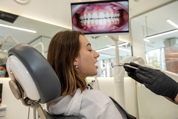 Over de schouder aanzicht van een tandarts die de tanden onderzoekt van een meisjespatiënt in een tandheelkundige kliniek Een vrouw onderzoekt haar tanden bij een tandarts