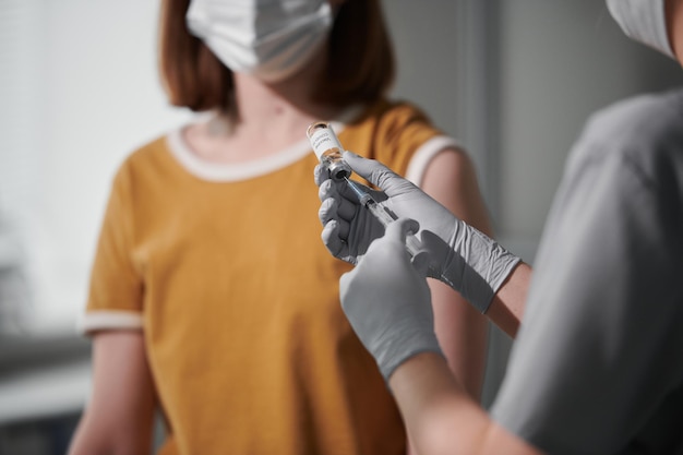 Over de schouder geschoten van onherkenbare vrouw die in de dokterspraktijk zit te wachten op een vaccininjectie