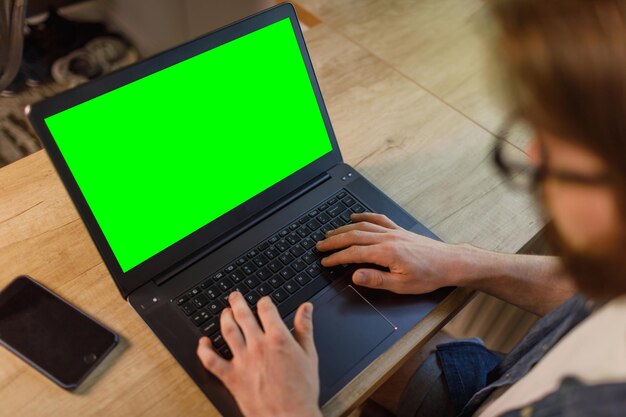 Over de schouder shot van een man die typt op een computerlaptop met een groen sleutelscherm