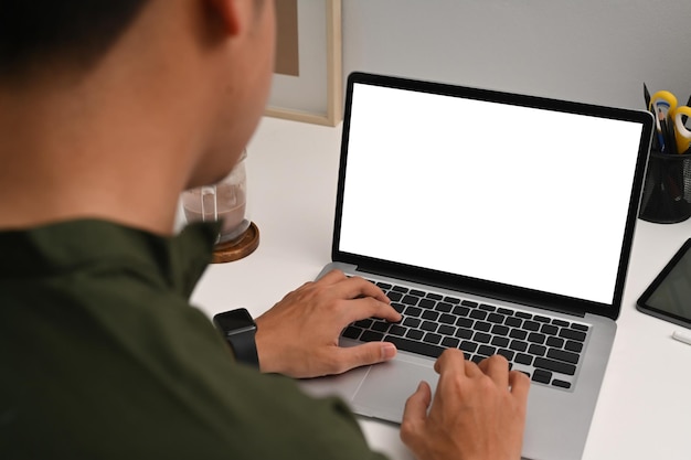 Over schouder bekijken jonge man met behulp van computer laptop op witte tafel