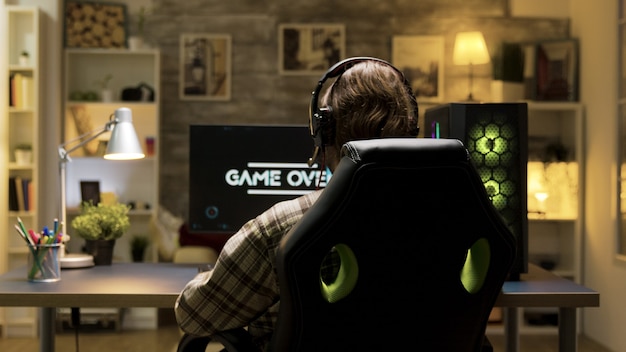 Over schouder shot van man na verlies bij videogames op computer met koptelefoon op. Game over tijdens het spelen van games.