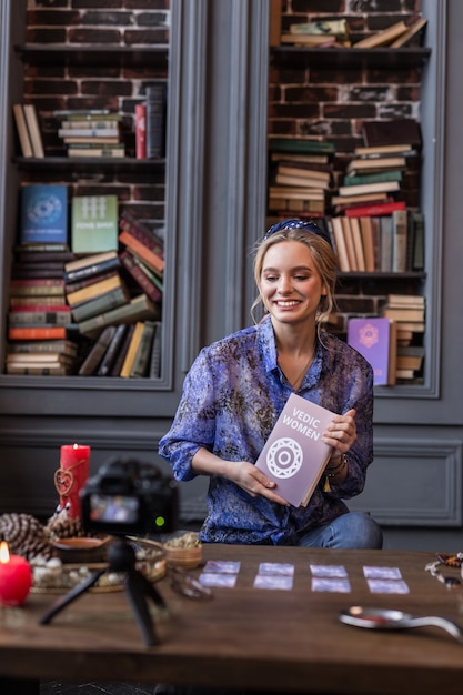 Over vedische vrouw. Vrolijke jonge vrouw die lacht terwijl ze een interessant boek voor de camera houdt