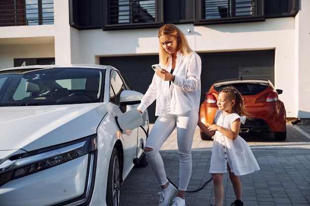 Overdag samen staan Wachten op een lading Jonge vrouw met haar dochtertje is met hun elektrische auto buiten