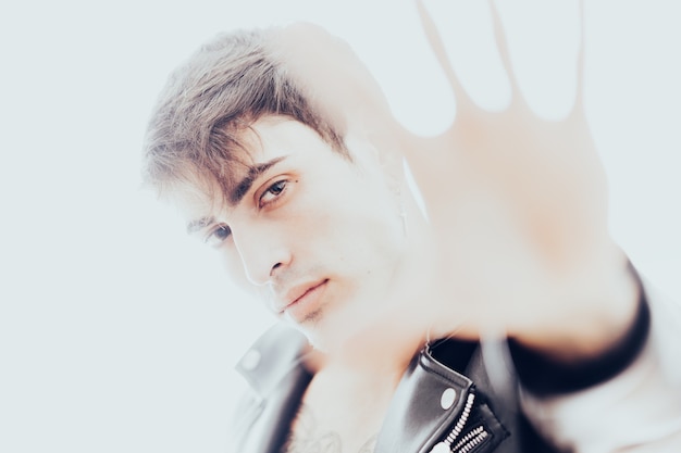 Overexposed studio photo of a young man with leather jacket\
covering the camera with his hand to hide his face.