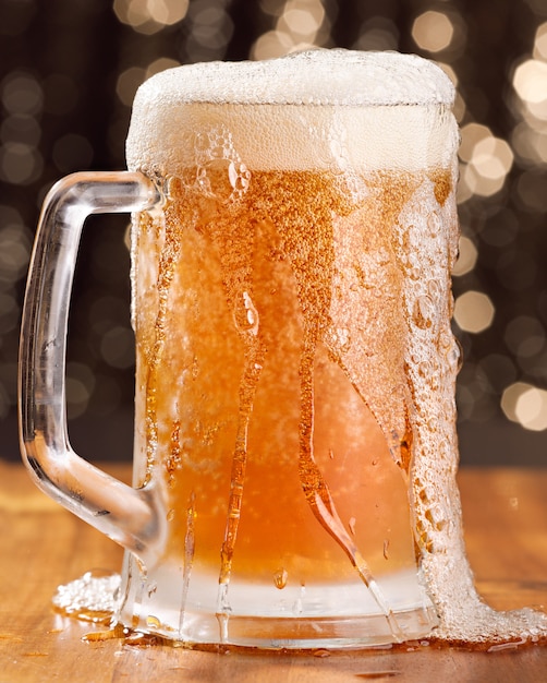 Overflowing mug of beer on wooden table