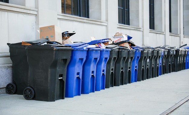 переполненный мусорный бак рядом с мусорными баками символизирует важность надлежащего обращения с отходами