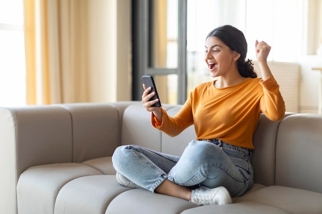 Overgelukkige Indiase vrouw met smartphone in de hand die succes thuis viert